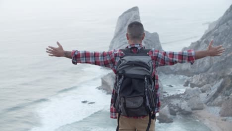 man is spreading his arms on top of a cliff looking over the sea