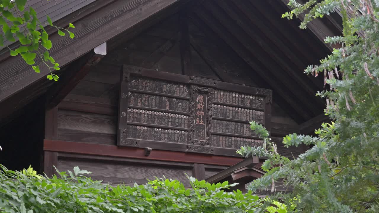 A close-up of a traditional Japanese wooden building's gable, featuring a richly carved decorative panel framed by dark timber and green foliage.
