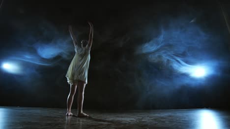 elegant ballerina jumping and dancing in barefoot and white loose oversize dress in studio. with smoke.