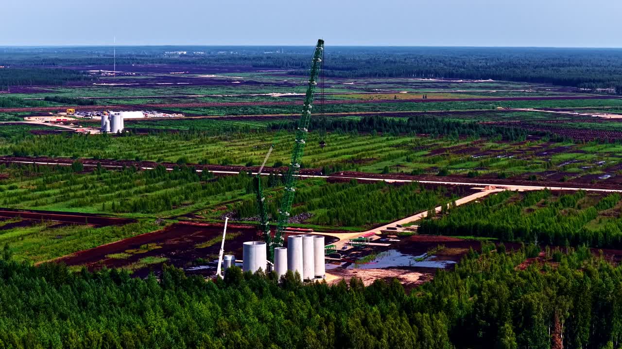 Aerial shot of cranes at work in construction in between a lush green field