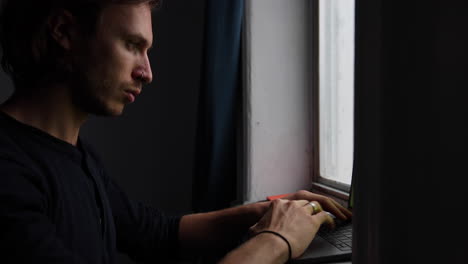 young man types on his laptop with a nice soft light hitting his face