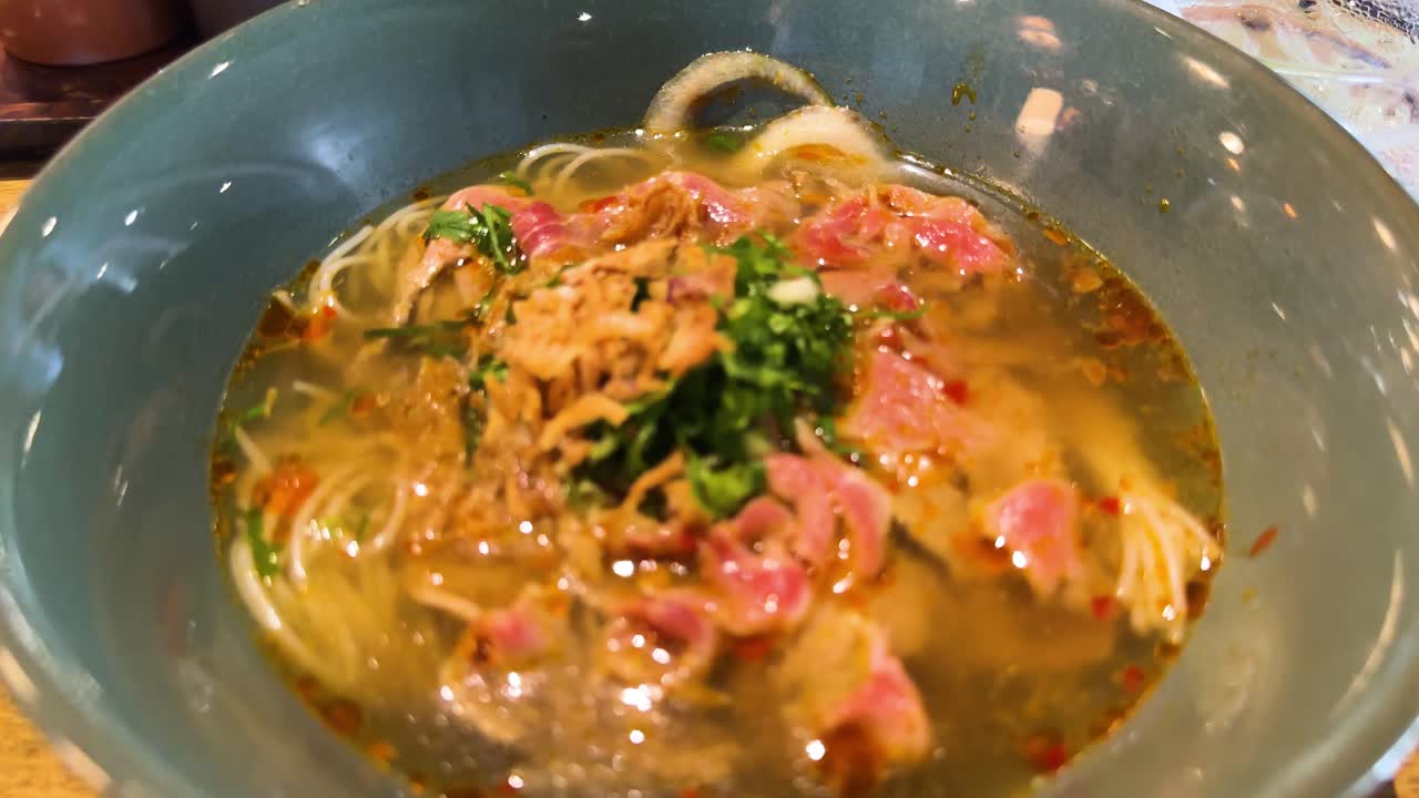 A steaming bowl of Vietnamese pho with beef, herbs, and noodles in a vibrant restaurant setting