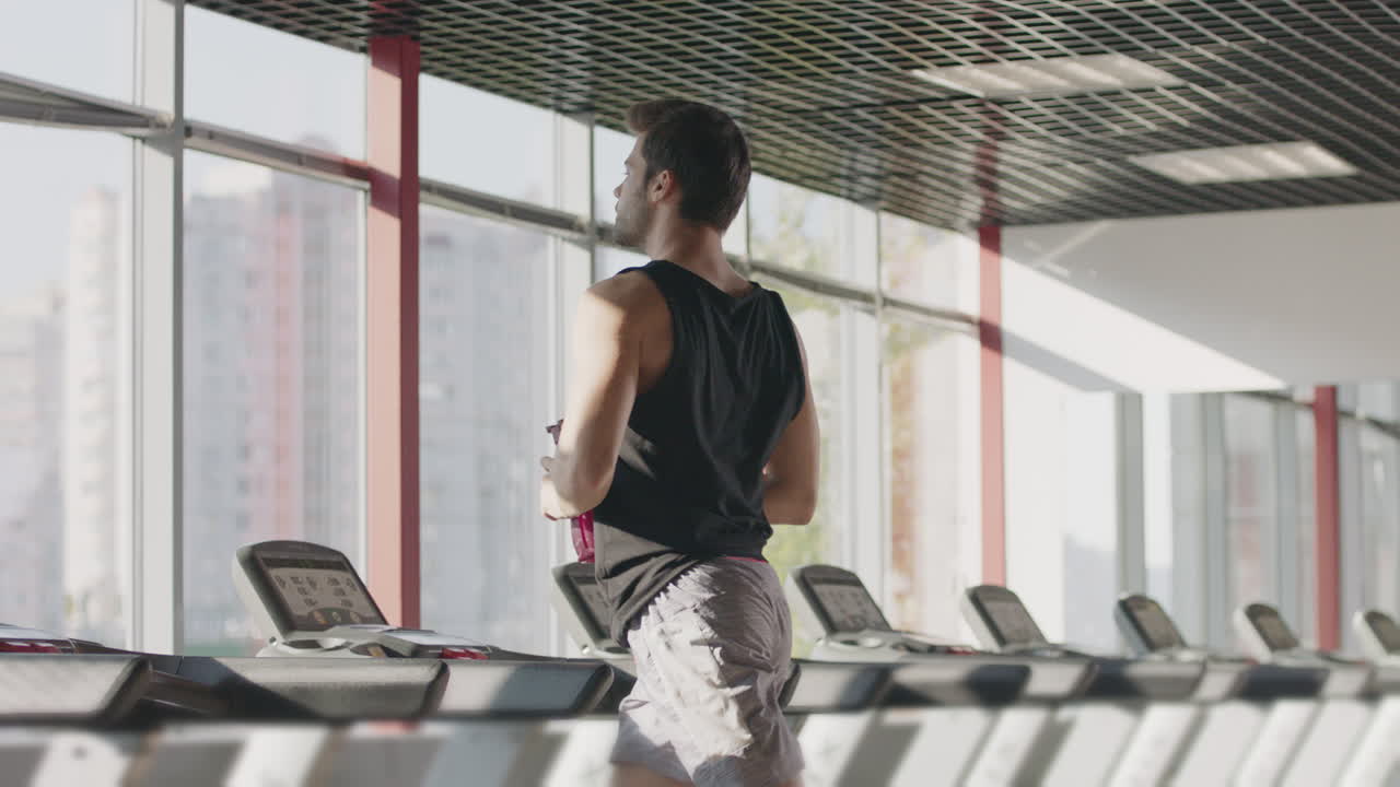 Runner man drinking water from bottle at intensive training on treadmill machine