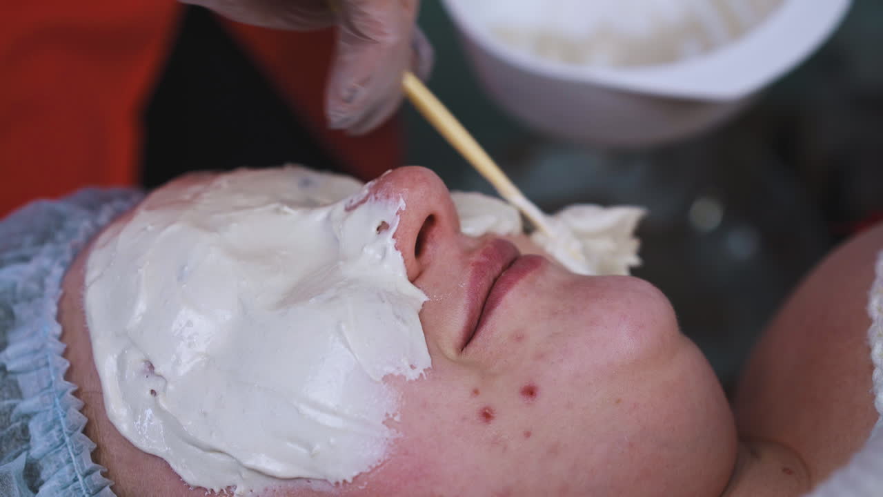 큰 여자가 알기네이트 마스크를 적용하는 화장품 전문가와 대화합니다.