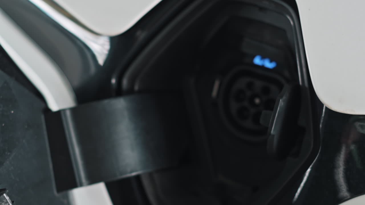 Man plugging in charger into an electric car, blue flickering light in the socket. Slow motion
