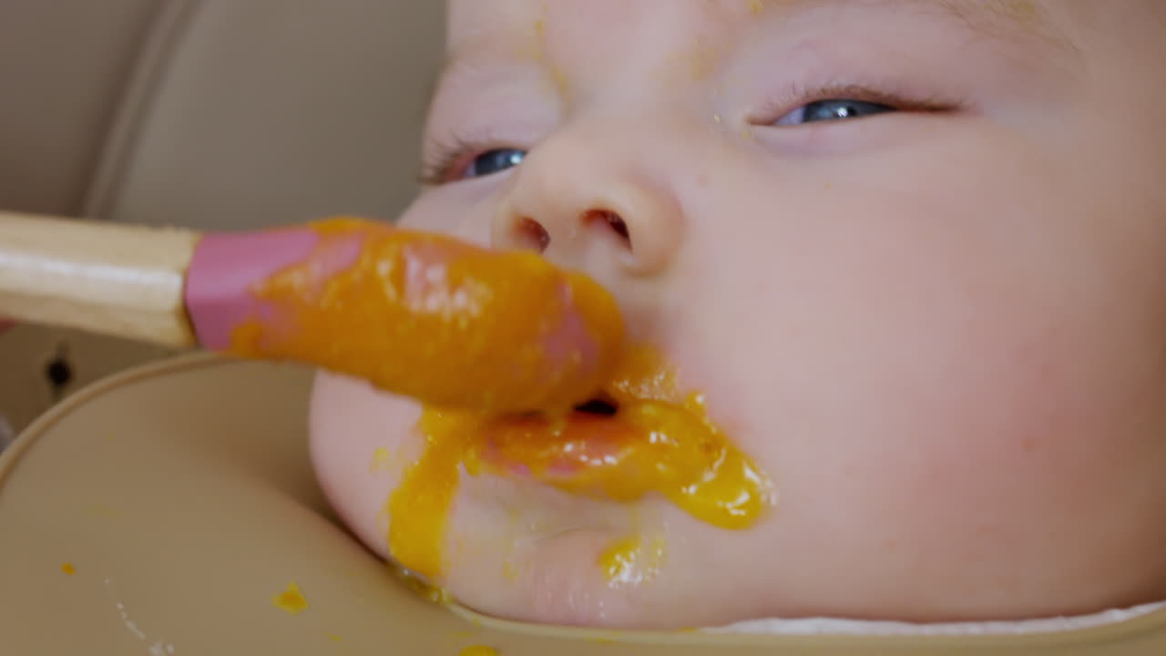 スプーンで離乳食を与えられている赤ちゃんのクローズアップ。顔の細部と穏やかな表情が見える。