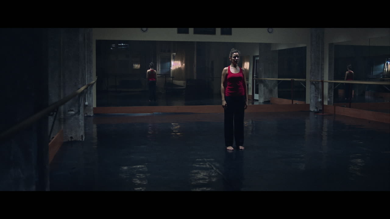 A young woman practices modern dancing and ballet in a moody room full of mirrors