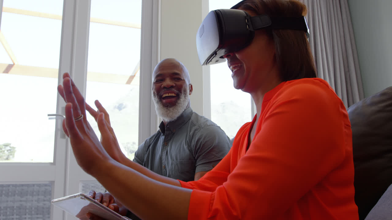Side view of mature black woman gesturing and using virtual reality headset in comfortable home 4k