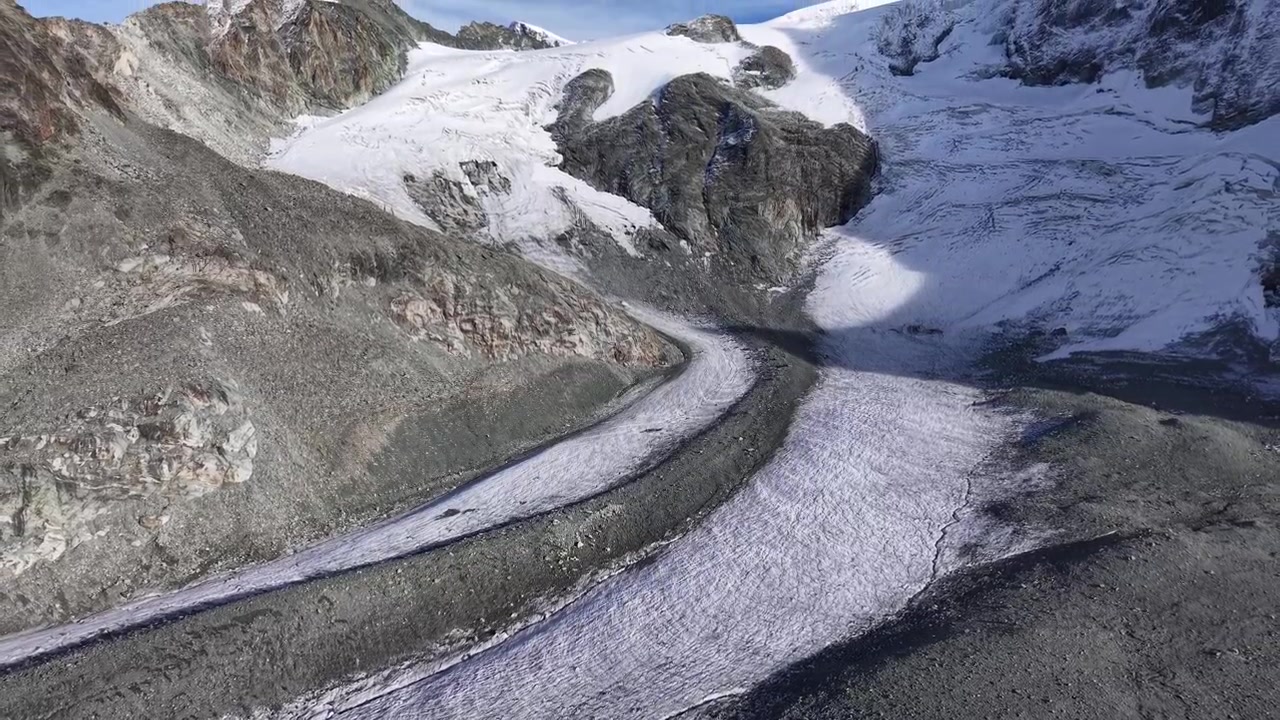 Aerial flyover next to the Glacier de Cheilon on a sunny summer day in the Swiss Alps with a pan up view towards the mountain peaks of Arolla such as Mont Blanc de Cheilon