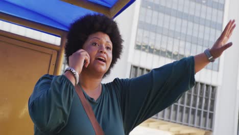 plus size biracial woman talking on smartphone and hailing taxi in city