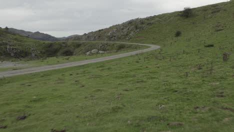 Drone-flying-at-low-altitude-over-green-meadows-and-rural-road,-Col-Inharpu,-Basque-Pyrenees,-France