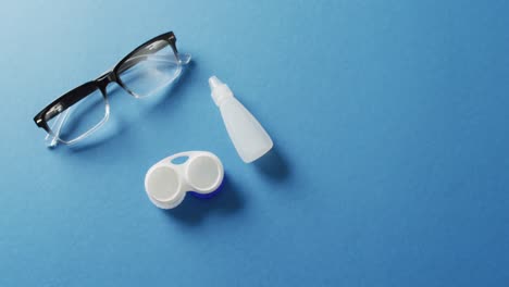 Video-of-pair-of-glasses,-contact-lenses-case-and-solution-on-blue-background-with-copy-space