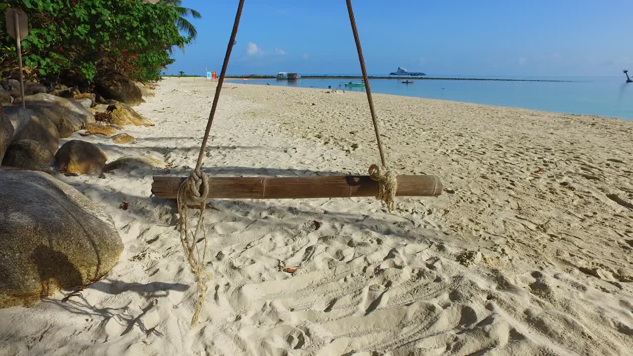 balancín todavía vacío cerca de los acantilados de piedra caliza sobre la arena blanca de la playa exótica, superficie del mar en calma que refleja el cielo azul brillante