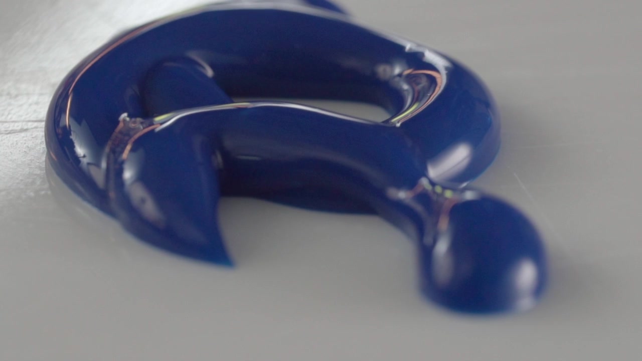 Macro primo piano di vernice acrilica blu lucida che forma una curva su una superficie chiara, evidenziando la texture liscia, la finitura riflettente e il ricco colore blu intenso.