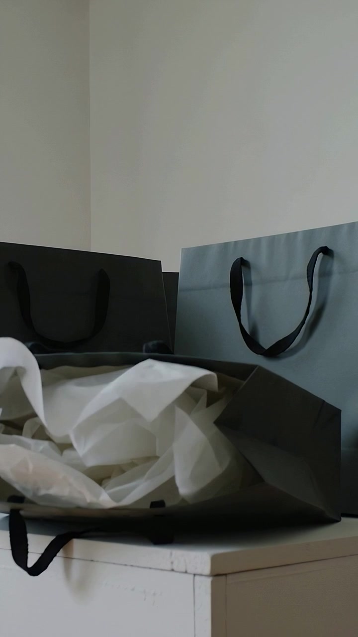Vertical video: Pulling tissue paper tipping front gray gift bag onto white cabinet, collapsing