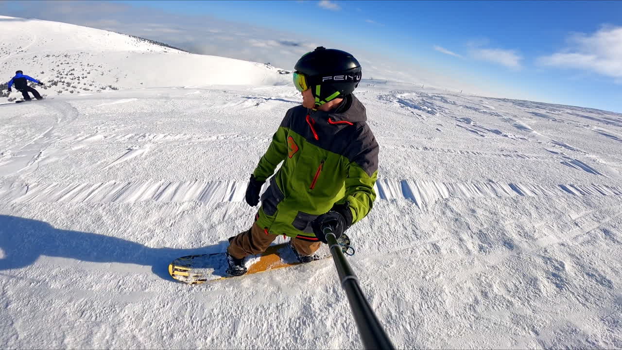 Sportsman in protective helmet taking selfie of his ride on the snowboard. Snowy slopes of the mountains at backdrop.