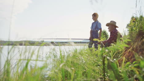 cute teen boy spending good time inthe nature with his grandpa while they ar angling in a lake