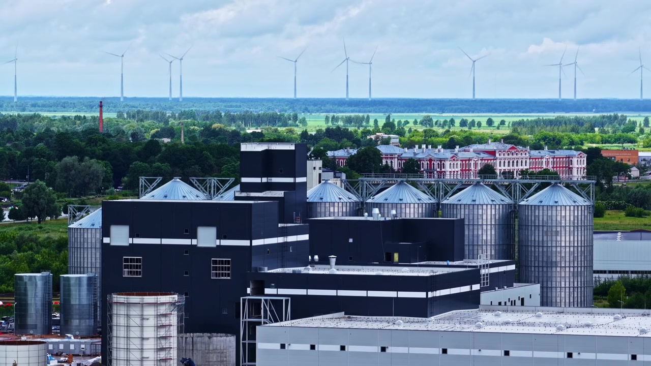 Industrial processing plant with storage silos and renewable energy turbines beyond in distance, timelapse
