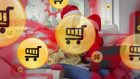animación de iconos de carretillas de compras en línea sobre madre y hija caucásicas en navidad