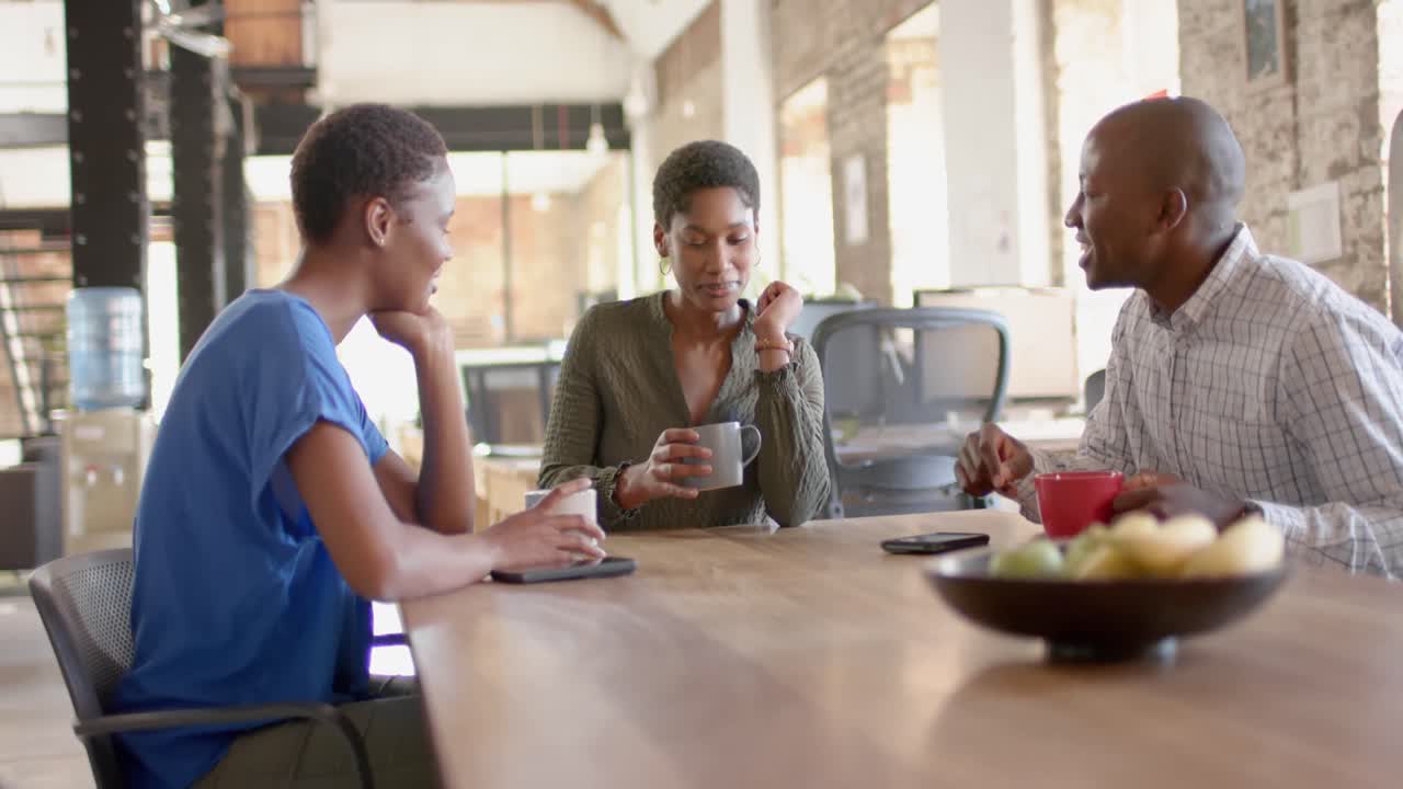 Felici colleghi afroamericani che parlano e bevono caffè in un ufficio creativo, al rallentatore