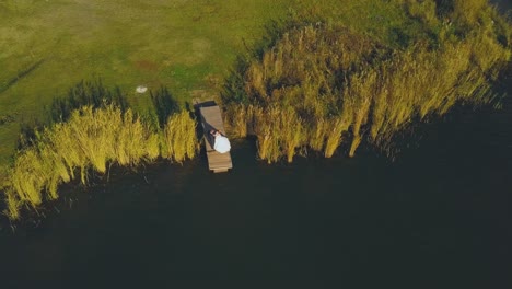 newlywed-couple-stands-on-pier-near-river-aerial-view