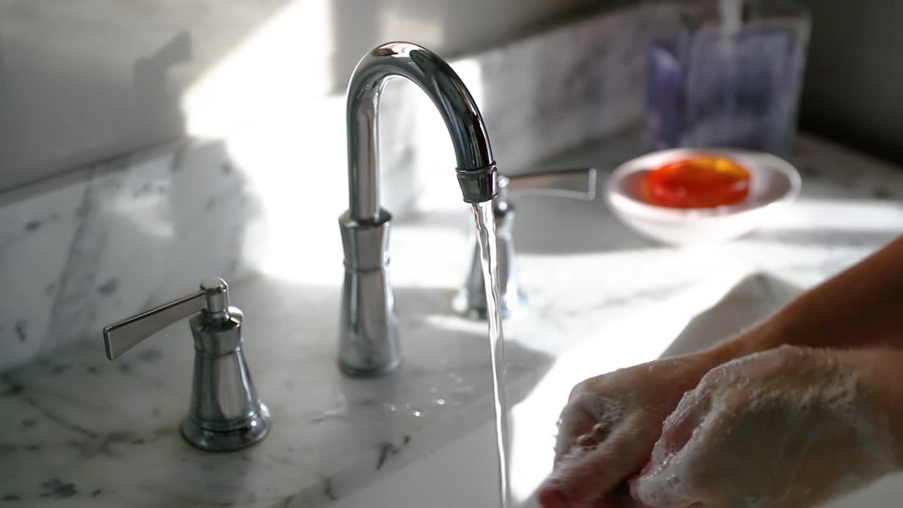 Primo piano di un uomo che si lava le mani in un bagno soleggiato in slow motion