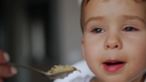 adorable baby face with some food around his mouth. child refuses to eat given food turning his head away. extreme close up.
