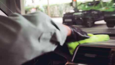 engineer wearing black gloves and using green microfiber cloth to clean up car dashboard and window