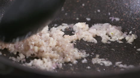 close up of frying shallots and garlic with oil in a black pan, caramelizing melting fried shallots and garlic