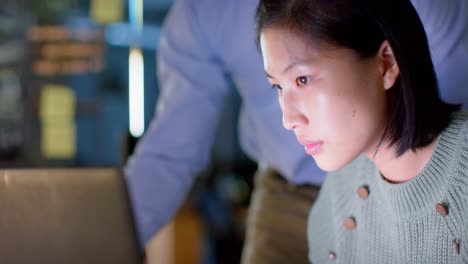 Focused-diverse-male-and-female-colleague-talking-and-using-computer-at-night-in-office