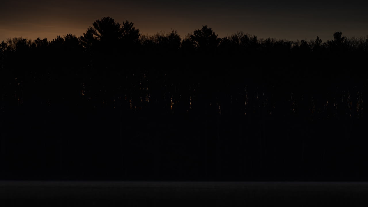 Time-lapse of sunrise through the trees on the far side of a small lake in northern Michigan