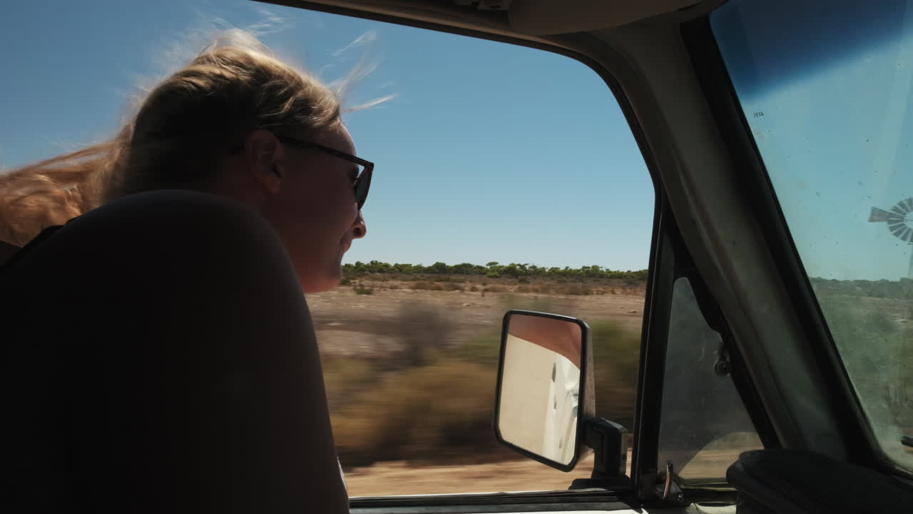 Young woman raising hand out of window and feeling free during bus ride in Australia