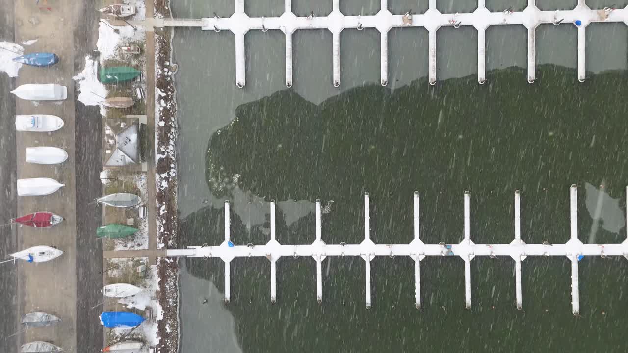 Top down aerial view tracking a frozen dock in the winter while snowing.