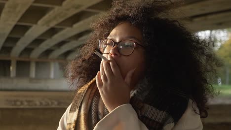 mujer negra fumando un sigaret afuera debajo de un puente durante su caminata de otoño