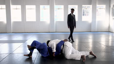 practicing judo, athletes grappling on mat in martial arts uniforms with coach observing