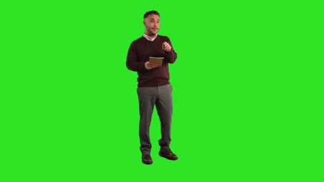 Full-Length-Studio-Portrait-Of-Mature-Male-Teacher-With-Notebook-Talking-To-Class-Standing-Against-Green-Screen