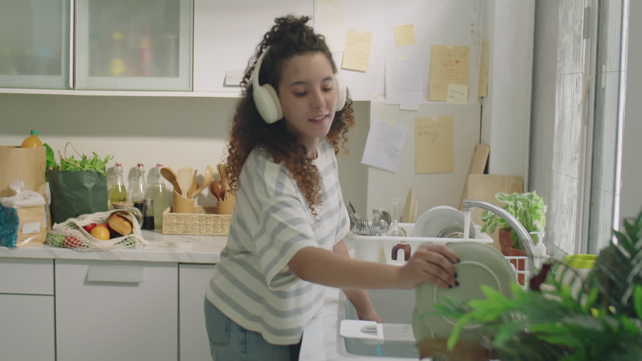 Garota ouvindo música com fones de ouvido e lavando a louça