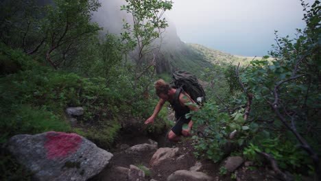 experienced male hiker with a large backpack easily climbing a steep rocky trail at mount donnamannen, nordland, norway