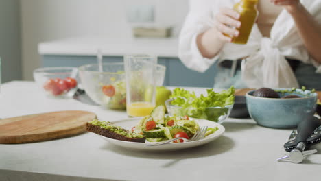 close up of woman hand pouring honey mustard dressing into plate with fresh salad and avocado toast