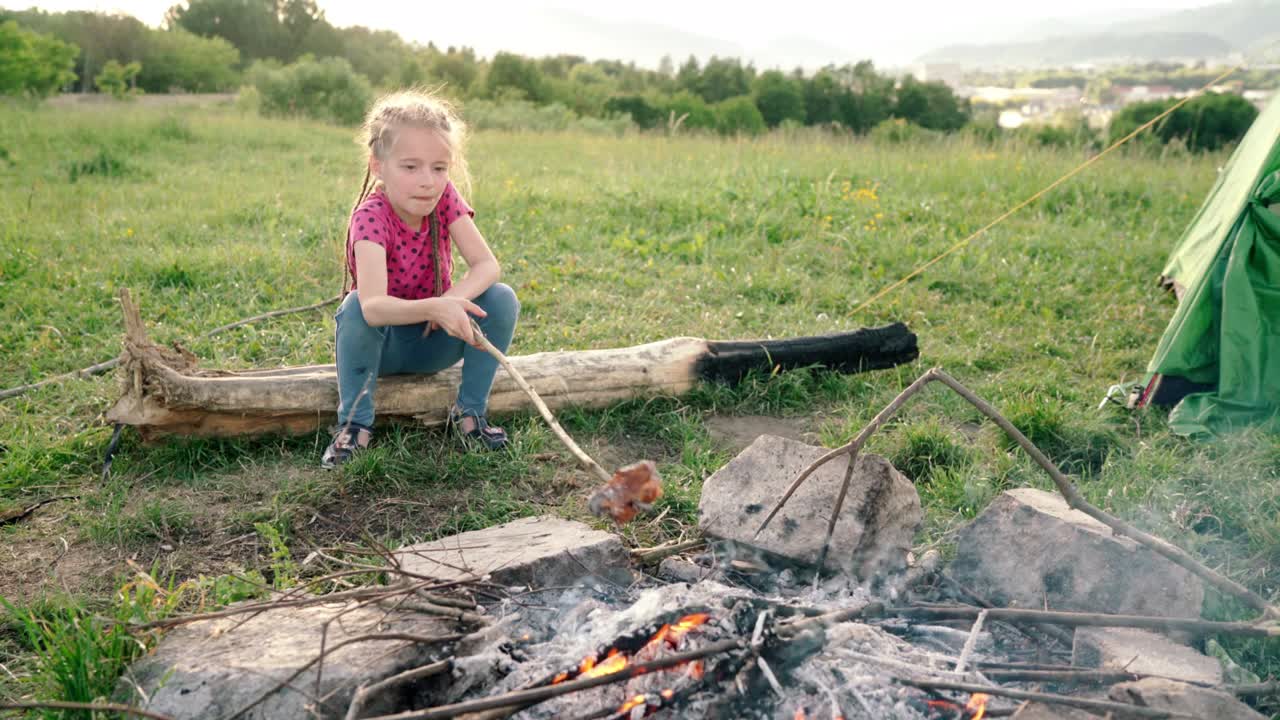 혼자 나무 위에 앉아 텐트 캠프에서 캠프 불 불꽃 위에 소시지를 고있는 어린 소녀 가족 야외 피크닉 활동 개념 4k 영상
