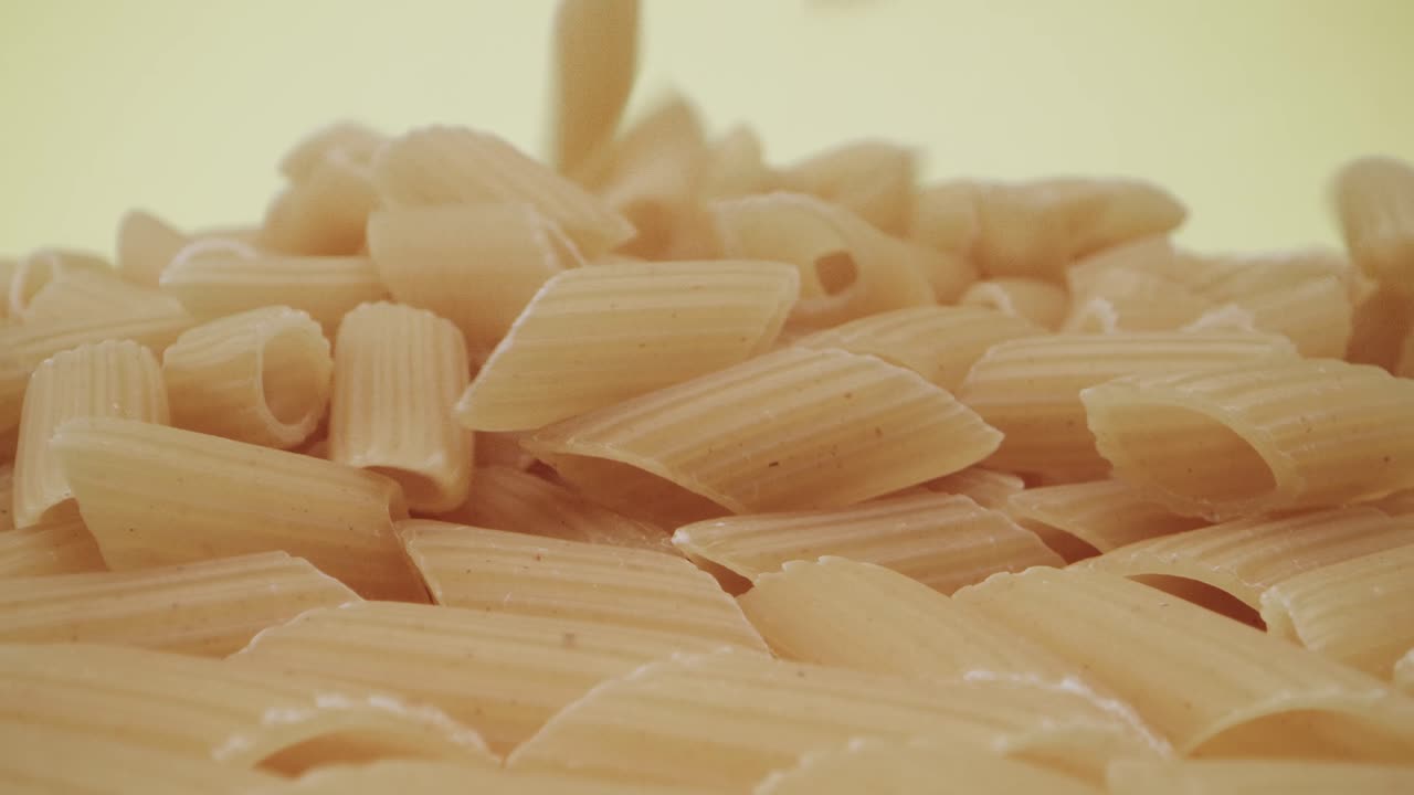 imágenes macro de sonda en tiempo real de la caída de pasta mezze penne rigate sobre fondo amarillo
