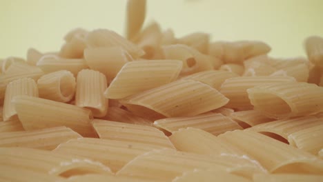 imágenes macro de sonda en tiempo real de la caída de pasta mezze penne rigate sobre fondo amarillo