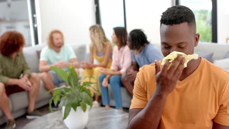 Emotional-man-crying-and-diverse-friends-talking-in-background-during-group-therapy-session