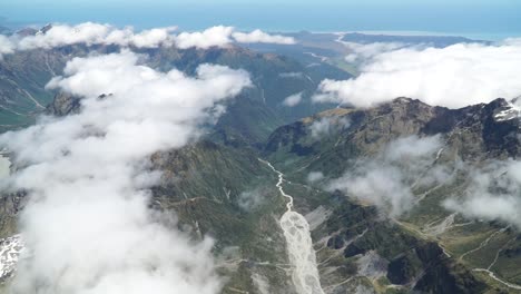 cámara lenta: toma aérea desde un vuelo panorámico sobre el glaciar fox de la costa oeste, el monte aoraki cook, el parque nacional con nubes, las montañas rocosas nevadas y el océano en el fondo