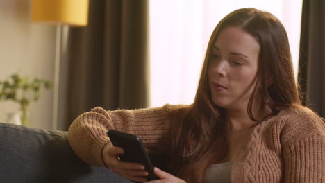 woman sitting on sofa at home using mobile phone to check social media message and scrolling online 13