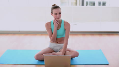 Fittes-Model-Sitzt-Auf-Trainingsmatte-Mit-Ihrem-Laptop