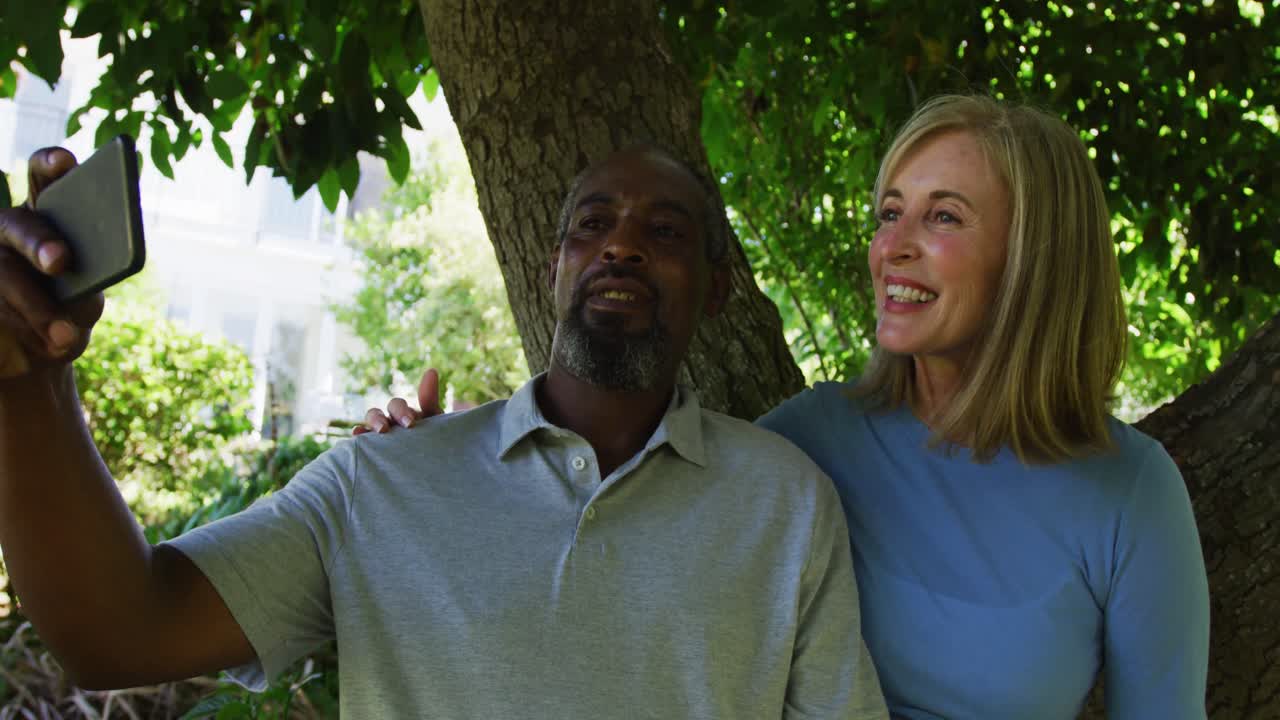 diverse oudere koppel in de tuin nemen selfie zitten onder een boom en glimlachen