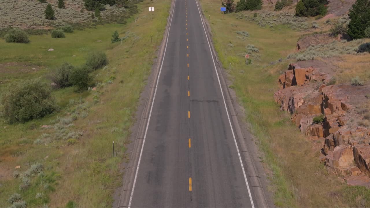 A car drives down a remote road through mountains and valleys on a sunny day in Wyoming