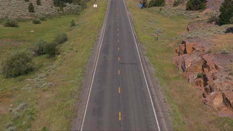 a car drives down a remote road through mountains and valleys on a sunny day in wyoming