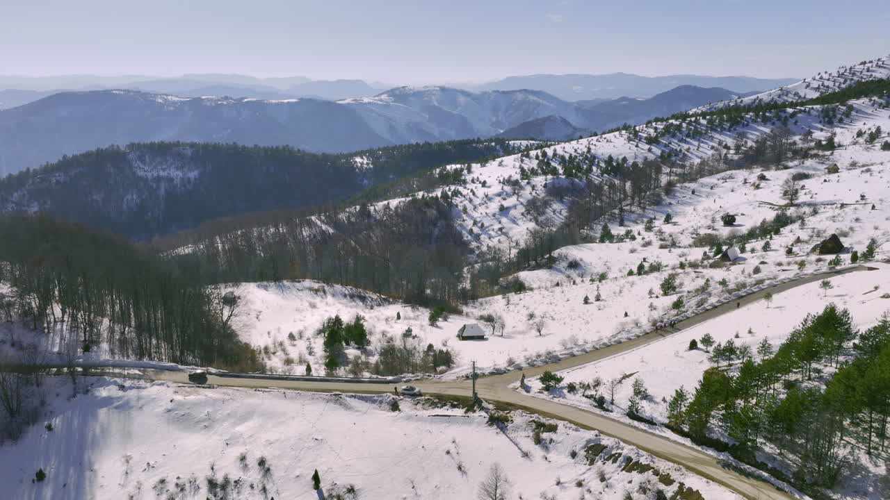 Aerial view of a winding road and remote cabin in a vast snowy mountain landscape